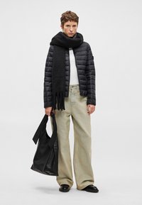 Juodas pūkinis švarkas ant balto marškinio, kreminės spalvos platėjančios kelnės, juodas šalis su kutais ir juoda odinė rankinė. Glotnios tekstūros, laisvas dizainas.