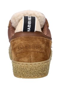 Zapatillas de ante marrón con suela de goma texturizada, forro de borreguito y una etiqueta negra en el talón que presenta el texto blanco "SHABBIES".