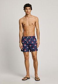 Moške kopalne hlače z mornarsko modrim ozadjem in rdečim vzorcem čolnov. Narejene so iz lahkotnega materiala; vključujejo elastični pas in vrvico.