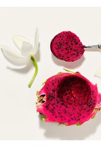 Fruit du dragon rose vif coupé en deux avec des graines noires, une cuillère prélevant une moitié, et une fleur blanche sur un fond clair.