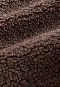 Tessuto in pile marrone con una superficie morbida e testurizzata, caratterizzato da piccole fibre arrotondate che creano un aspetto soffice.