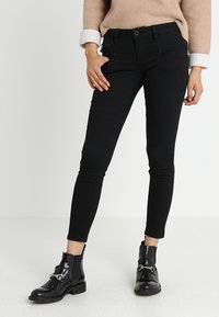 Jeans skinny de denim negro con una cintura alta, que cuentan con bolsillos frontales y una textura sutil. Combinados con botas de tobillo.