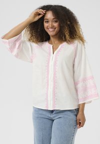 Blusa bianca in lino con accenti ricamati rosa lungo il collo e le maniche a campana, dotata di una parte di bottoni e di una vestibilità rilassata.