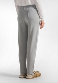 Grijze gebreide joggingbroek met een relaxte pasvorm, elastische tailleband en een enkele achterzak. Gecombineerd met beige donzige pantoffels.