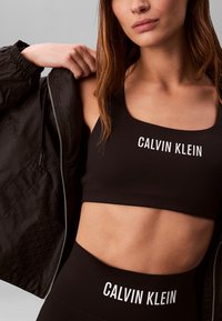 Sujetador deportivo negro y leggings de cintura alta de Calvin Klein, con texto de logo en blanco. Material suave y elástico con costuras mínimas.