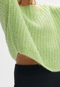 Pull vert doux en maille avec une texture côtelée, manches larges et encolure arrondie, associé à un bas noir ajusté.