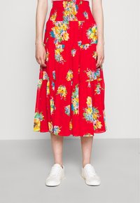 Roter Midi-Rock mit Blumenmuster und gesmoktem Bund; leichtes Material, gestuftes Design mit bunten Blumen; kombiniert mit weißen Sneakern.