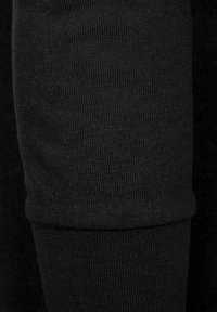 Černá tkanina s vroubkovanou strukturou a hladkým povrchem, která ukazuje detailní záběr na její pružnost a švy.