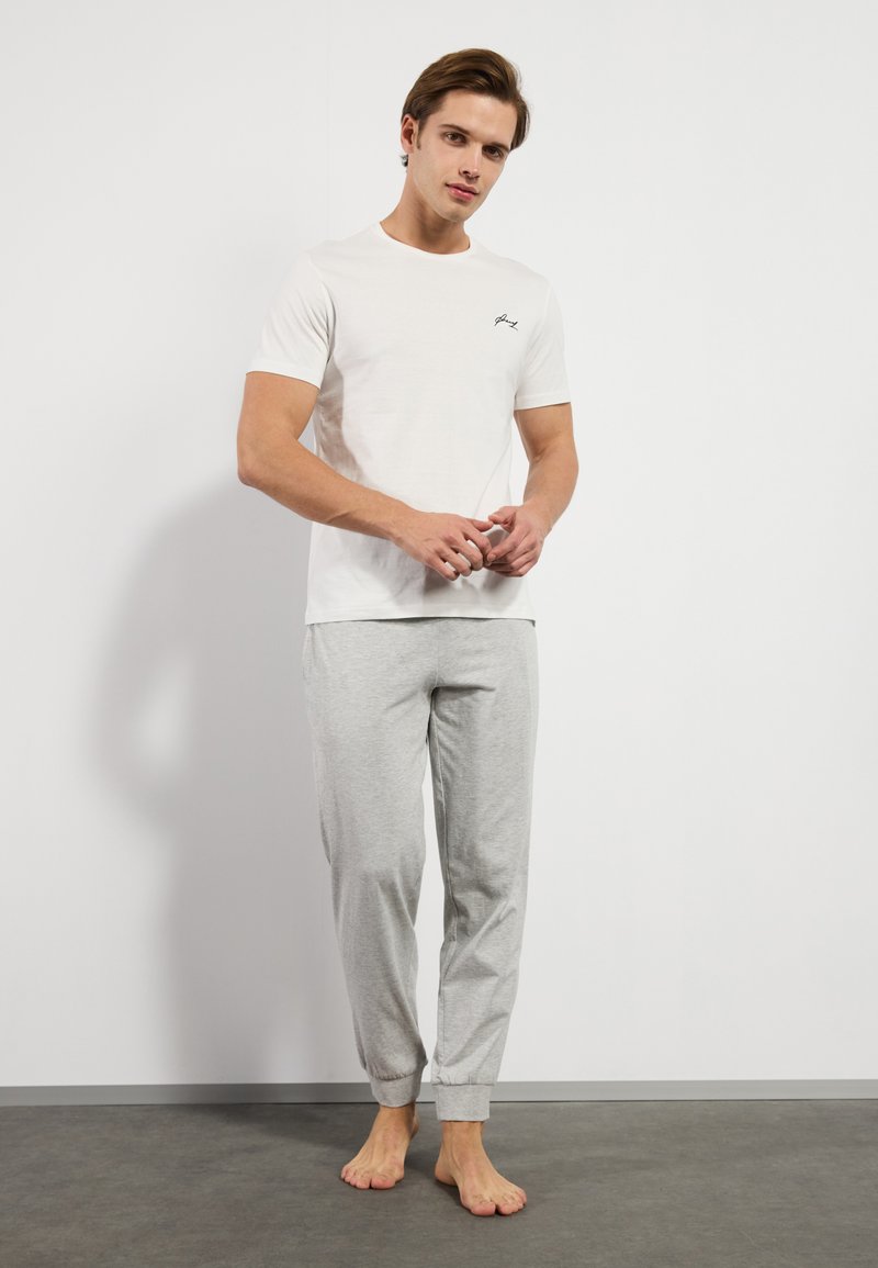Hvit bomulls t-skjorte med korte ermer og en liten svart logo på brystet, sammen med lysegrå joggebukser med elastisk liv.