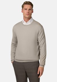 Pull en tricot beige avec un col rond, des manches longues et des poignets côtelés, associé à un pantalon gris à carreaux. Texture lisse, design minimal.