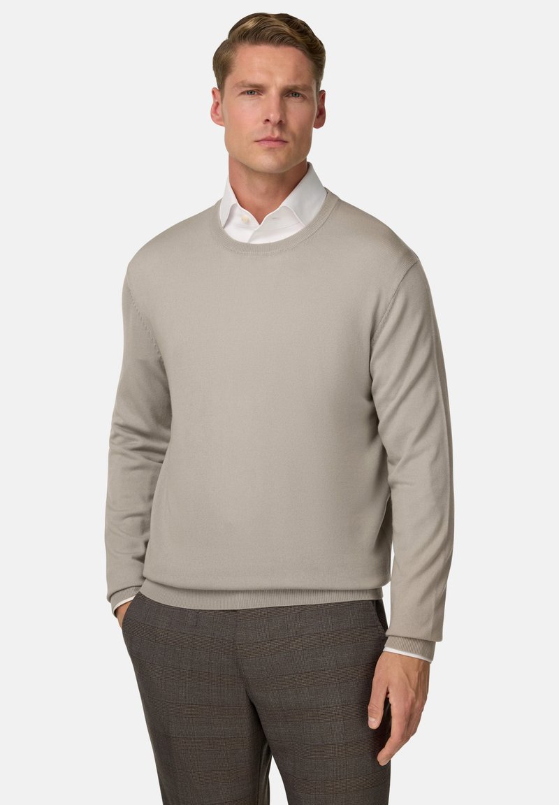 Pull en tricot beige avec un col rond, des manches longues et des poignets côtelés, associé à un pantalon gris à carreaux. Texture lisse, design minimal.