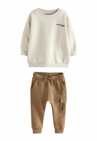 Krämfärgad sweatshirt med rund halsringning och svart text; kombinerad med bruna sweatpants med elastisk midja och sidoficka.
