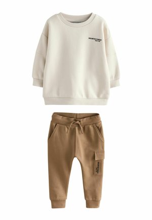 Cremefarbener Sweatshirt mit rundem Ausschnitt und schwarzem Text; kombiniert mit braunen Jogginghosen mit elastischem Bund und Seitentasche.