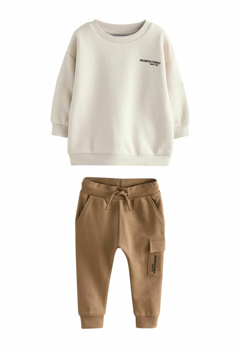 Krämfärgad sweatshirt med rund halsringning och svart text; kombinerad med bruna sweatpants med elastisk midja och sidoficka.