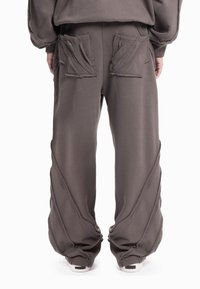 Zakken, donkergrijze broek gemaakt van zachte stof, met unieke getextureerde zakkleppen en naden die diagonaal langs de buitenkant van de benen lopen.