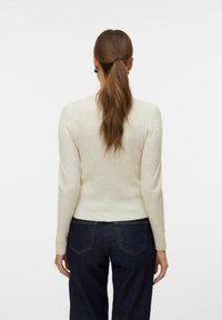 Rippendes, langärmliges Oberteil in heller Cremefarbe, figurbetonte Silhouette, mit Rundhalsausschnitt und leicht verkürztem Saum, kombiniert mit dunklen Jeans.