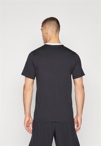 Zwarte katoenen T-shirt met korte mouwen en een witte ronde hals, met een relaxte pasvorm en een zachte textuur. Achteraanzicht met subtiele stiksels.