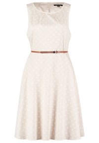 Un vestido sin mangas, beige con lunares blancos, que cuenta con un cinturón en la cintura y una cremallera en la parte posterior. La tela tiene una textura suave.