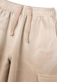 Pantalones de chándal beige hechos de una tela suave, con una cintura elástica y cordones, y un detalle bordado de "Utopia" en el lateral.