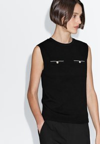 Black sleeveless top in soft fabric with a crew neck, featuring two decorative pockets with silver accents at the front.