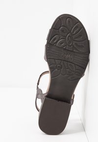 Sandale noire avec une semelle texturée présentant un motif floral, une sangle ajustable et un logo 'Soft FLEX'. Design épuré et pratique.