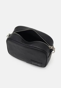 Borsa in pelle nera con trama, dotata di zip argentata, caratterizzata da una forma curva e un'etichetta branded sul lato. Aperta per mostrare l'interno.