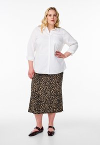 Chemise blanche à manches retroussées, accompagnée d'une jupe mi-longue à imprimé léopard. Chaussures plates marron avec des accents de boucle.