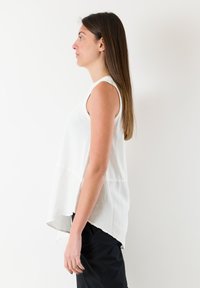 Witte mouwloze top met een ontspannen pasvorm, voorzien van een gelaagd ontwerp en een iets langere achterkant, gedragen met zwarte broek.