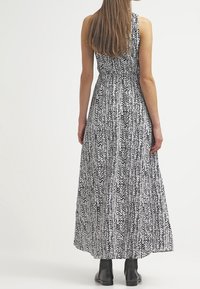 Black and white patterned maxi dress with a fitted waist, sleeveless design, and flowing fabric. Paired with black ankle boots.