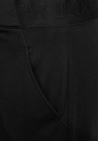 Svarta joggers i bomullsblandning med midjeband med präglad text och en sidoficka, som visar en slät, matt yta.