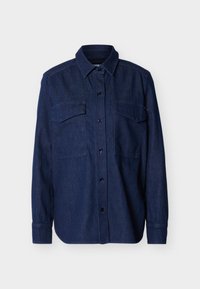 Πουκάμισο μακρυμάνικο από σκούρο μπλε τζιν με κουμπιά, με μυτερό γιακά και δύο τσέπες στο στήθος με καπάκια, σε μονόχρωμο φόντο.