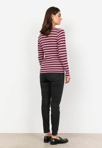 Maglietta a maniche lunghe a righe in tonalità di viola e rosa, abbinata a jeans neri aderenti e mocassini neri, vista da dietro.