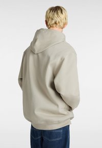 Lichtbeige hoodie met een trekkoordcapuchon en ribgebreide mouwen. Zachte katoenmix met een relaxte pasvorm. Donkerdenim jeans zichtbaar eronder.