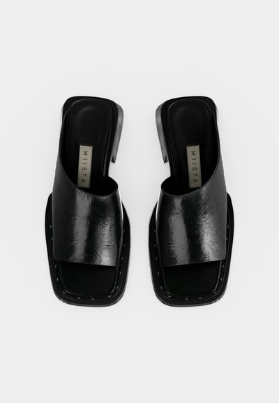 Ζευγάρι μαύρα δερμάτινα σανδάλια τύπου slip-on με ανοικτά δάχτυλα, τετράγωνες σόλες και χοντρά τακούνια, με ετικέτα "MIISTA" εσωτερικά.