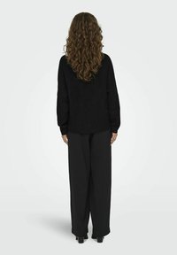 Black textured oversized sweater with long sleeves, paired with wide-legged black trousers. The outfit offers a relaxed fit and minimal design.
