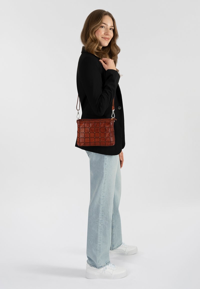 Borsa in pelle marrone con motivo a griglia, di media grandezza, con tracolla regolabile e dettagli in hardware argentato, abbinata a un blazer nero e jeans chiari.