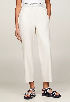 Pantaloni bianchi, leggeri, a vestibilità morbida, con cintura elastica e tasche laterali, abbinati a sandali neri e bianchi con cinturini.