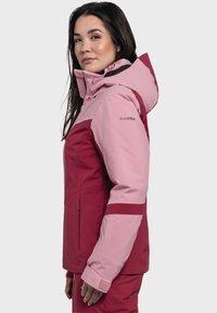 Pink and burgundy waterproof jacket with a hood, features contrasting sleeves, zippers, and a soft texture. Logo on shoulder.