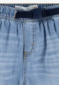 Pantalon en denim bleu clair avec ceinture élastique, ceinture réglable bleu marine avec boucle en plastique et étiquette de taille visible à l'intérieur.