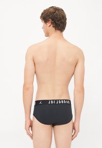 Schwarze Schwimmbrieftaschen mit einem weißen Markenbund, auf dem "JORDAN" steht. Glattes Material, körpernahe Passform und minimalistischer Stil.