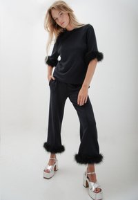 Zwarte gebreide top met nep bontaccenten op de mouwen, gecombineerd met zwarte broek met bont aan de boorden. Model draagt zilveren platform schoenen.