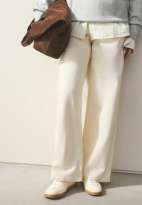 Plačios grietinėlės spalvos kelnės iš minkštos medžiagos, derinamos su baltomis sportbačiais. Pilkas megztinis ir rudas zomšinis krepšys papildytų aprangą.