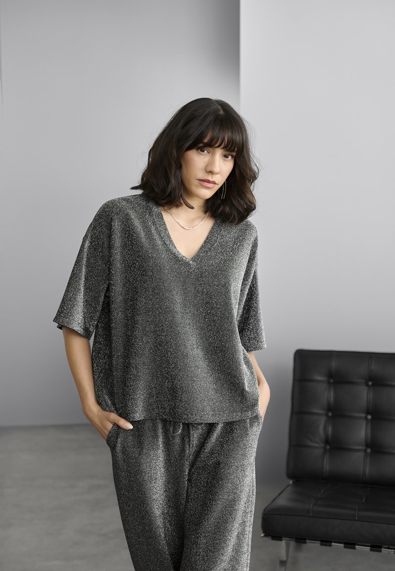 Gray shiny v-neck top with short sleeves, paired with matching gray pants. Soft texture with an oversized fit. Black leather chair in the background.