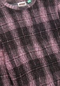 Nahaufnahme eines schwarz-pinken, strukturierten Guess Originals Shirts mit einem Karomuster und einem Eco Collection-Tag in der Nähe des Kragens.