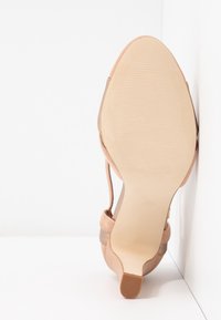 Chaussure à talons hauts beige pour femme vue de la semelle, montrant un dessous en cuir lisse et un petit embout de talon texturé.