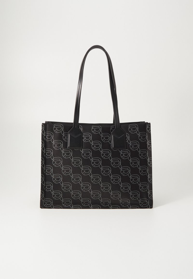 Zwarte tote bag met herhaaldelijk lijntekening gezichtenpatroon, met stevige zwarte handvatten en een rechthoekige vorm, gemaakt van duurzaam materiaal.