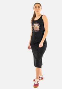 Vestido sin mangas negro con un estampado gráfico. Tela suave y elástica con un diseño a la altura de la rodilla. Combinado con zapatillas burdeos y blancas.