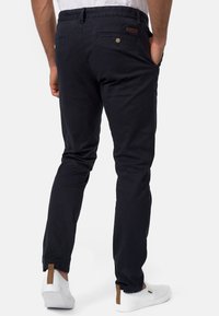 Chino in cotone blu navy con una vestibilità slim, dotati di tasche posteriori e dettagli con bottoni. Abbinati a scarpe slip-on bianche e una cintura texturizzata.