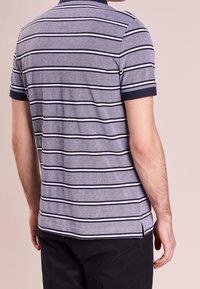 Polo rayé en bleu et blanc, à manches courtes, en tissu doux. Dispose d'un col marine, de fentes latérales à l'ourlet et d'un motif texturé.