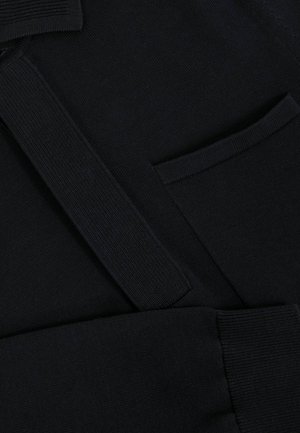 Tessuto a maglia blu navy scuro con cintura e polsini a coste, caratterizzato da una piccola tasca rettangolare.